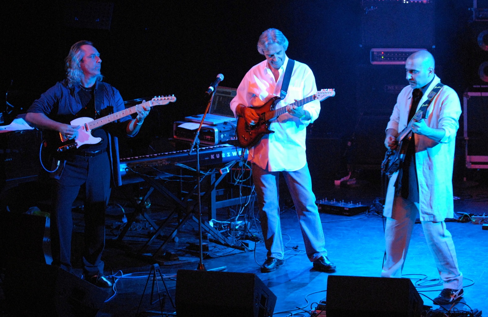 Trois guitaristes sur scène sous un éclairage bleu